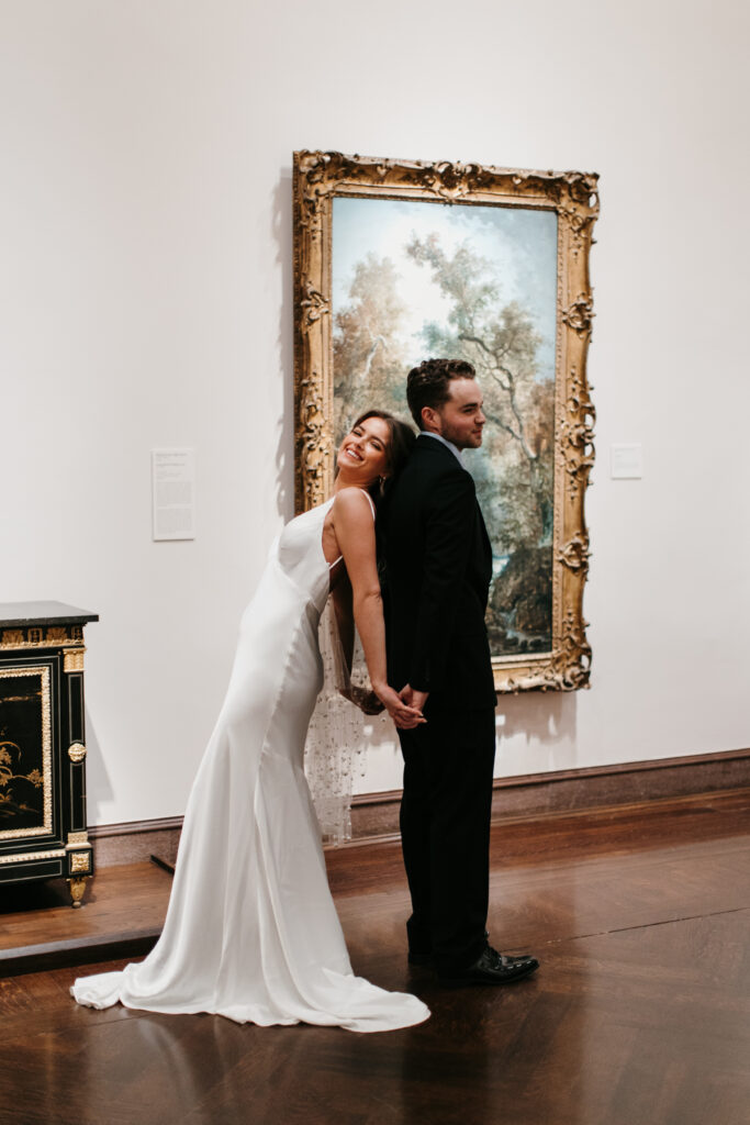 couple leaning back to back in front of painting