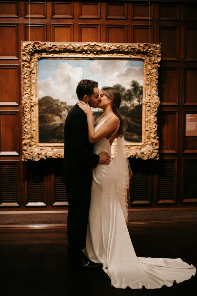 bride and groom share a kiss in front of painting